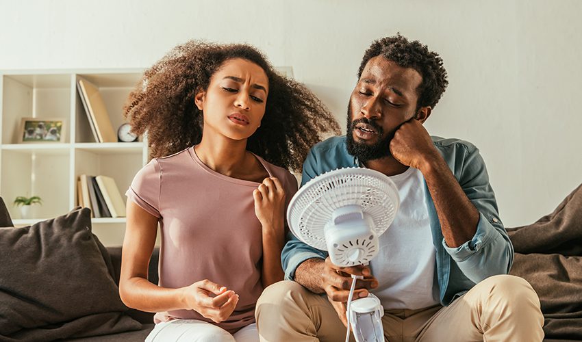 A man and woman try to cool off in front of a fan